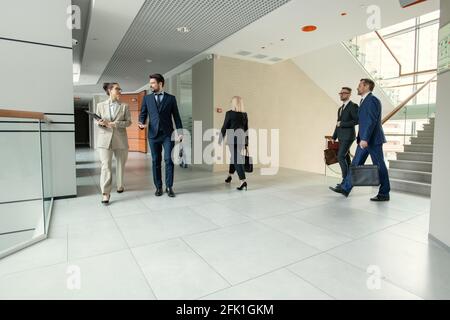 Contemporary office corridor full of business people hurrying to work: colleagues walking over corridor and discussing projects Stock Photo