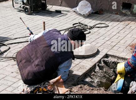 Dnepropetrovsk, Ukraine - 03.26.2021: Water utility workers open an old manhole and replace old rusty pipes with new ones. Stock Photo