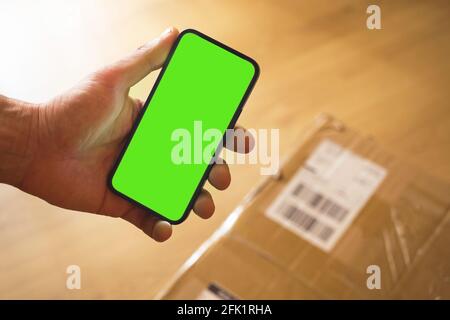 Concept of receiving big parcel at home, smartphone mockup green screen with place for your text advertising, man hold mobile phone while delivery ser Stock Photo
