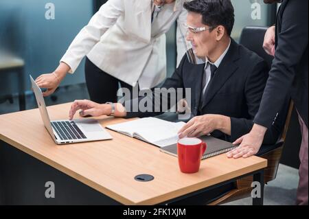 Happy asian female manager consulting and collaborating with colleagues working with laptop at desk in the office Stock Photo