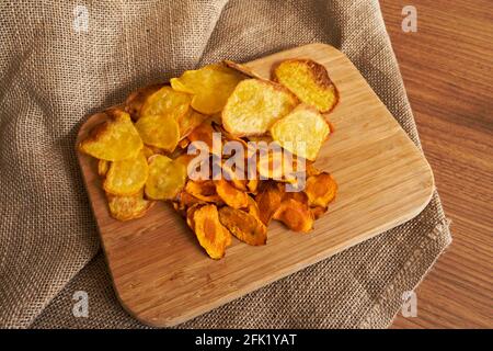 Fresh baked potato and carrot chips on a board and a sack under of them.Looks yummy. Homemade chips. Stock Photo