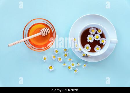 A cup of tea with chamomile and honey in glass bowl with wooden dipper on blue background. Top view, flat lay. Stock Photo