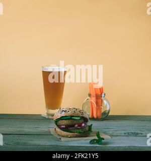 Healthy vegan hamburger and beer in a glass on wooden table. Orange wall background.