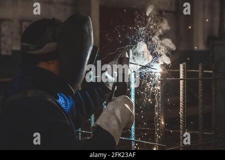 A masked working man is doing welding work on metal structures in a factory or industrial enterprise. Stock Photo