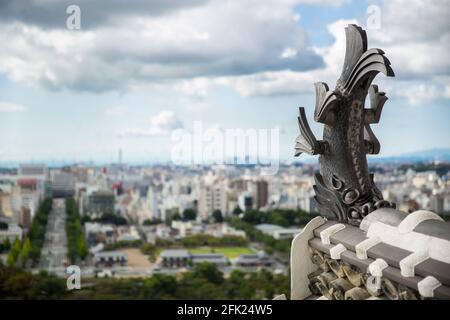 Koi carp Tiger headed fish statue on roof top of Himeji Castle with view of Himeji City (soft focus), Japan Stock Photo