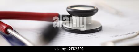 Red stethoscope lying on documents in clipboard in clinic closeup Stock Photo