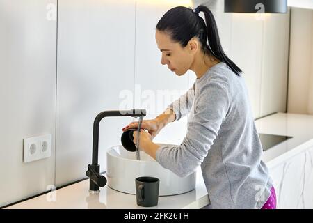 Caucasian woman washes dishes in kitchen sink. Stock Photo