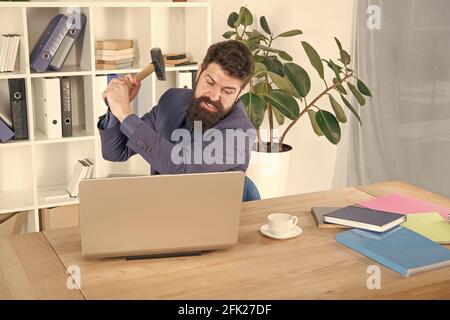 hate my job. dealing with error. overworked man crush laptop with hammer. frustrated computer user. businessman express anger. ready to smash. Office Stock Photo