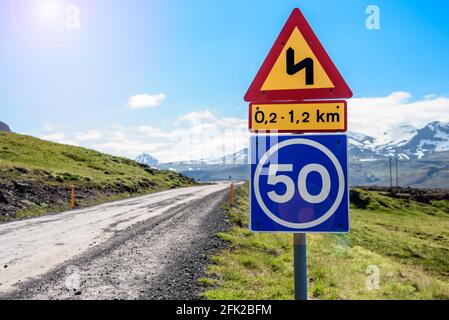 Triangular winding road warning sign with speed limit along a remote gravel mountain road on a sunny summer day Stock Photo