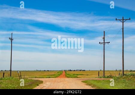 The road less traveled - a rural cross roads with a red dirt road leading forward over the horizon in farm country under very blue sky Stock Photo