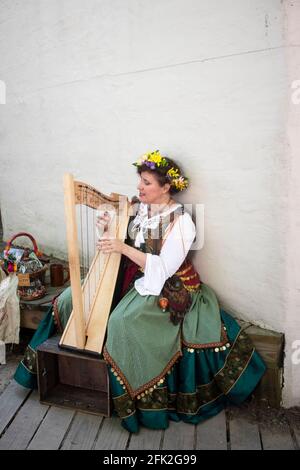 Woman in medival dress sitting on a bench playing a harp at Oklahoma Renaissance Festival Muskogee OK 5 13 2018 Stock Photo