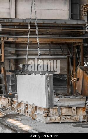 A large concrete plate on a lifting mechanism with a chain in the reinforcement production of an industrial enterprise. Stock Photo