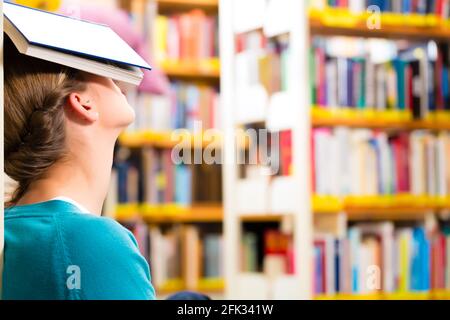 Student - Young woman in library with book learning, she is asleep Stock Photo