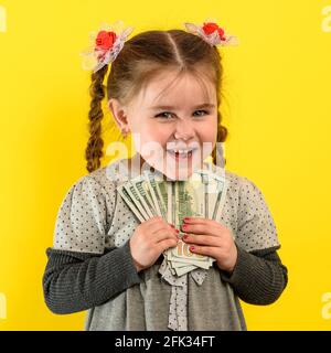 Children and financial responsibility, little girl on a yellow background with dollars in her hands, financial literacy in a child. Stock Photo