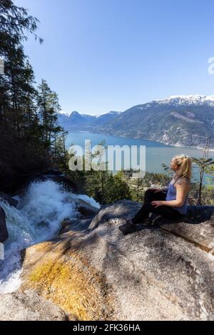 Adventurous Adult Woman is sitting on top of a Beautiful Waterfall Stock Photo