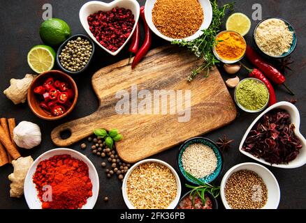 Various spices in a bowls and empty cutting board on black concrete background. Top view copy space. Stock Photo