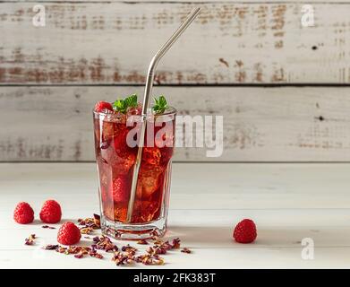 Cold sparkling hibiscus or karkade ice tea with lemon, mint, and raspberry in glass on a wooden table. Healthy drink. Stock Photo