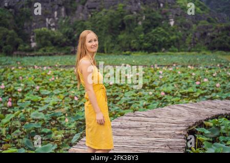 Young woman in a yellow dress on the path among the lotus lake. Mua Cave, Ninh Binh, Vietnam. Vietnam reopens after quarantine Coronovirus COVID 19 Stock Photo