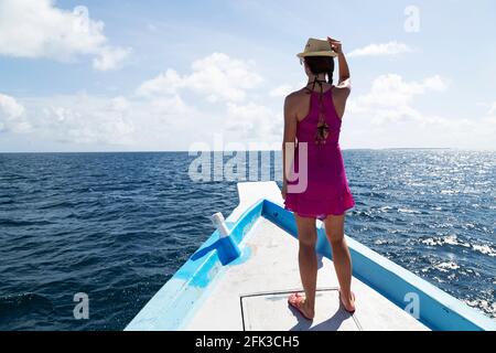 Woman holds her hat while standing on the deck of a wooden boat in the Maldives. The Maldives is a popular holiday tropical destination in the Indian Stock Photo