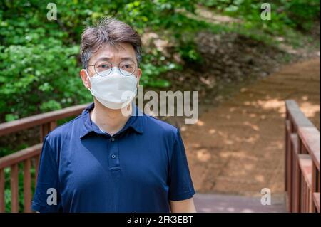 Middle-aged Asian man walking alone in a forest path wearing a face mask. Stock Photo