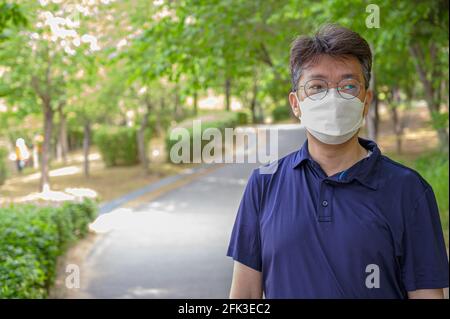 Middle-aged Asian man walking alone in a forest path wearing a face mask. Stock Photo