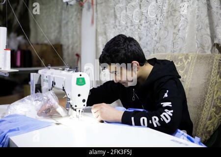 April 16, 2021, Gaziantep, Southeast Anatolia, Turkey: Gaziantep, Turkey. A 13 years-old boy works with his father at a sewing workshop in the Turkish city of Gaziantep. The workshop, which produces high quality garments and Coronavirus protective gowns, was established by Syrians who fled the war-torn country in search of safety. Syrians have suffered greatly from the conflict, the displacement, and the struggle to survive in another country, with children often having to work and missing out on school to contribute to their family's income (Credit Image: © Stringer/IMAGESLIVE via ZUMA Wire Stock Photo