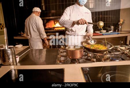 Chef adding sauce to vegetables in cooking pan Stock Photo