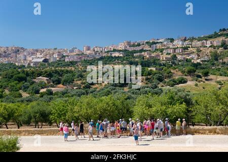Agrigento, Sicily, Italy. Tourists on the Via Sacra looking towards the city across landscape of olive and almond groves, Valley of the Temples.