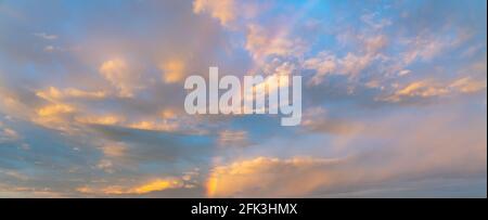 Sunset sky covered with gentle golden clouds and rainbow Stock Photo