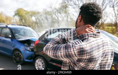 Young man rubbing neck in pain from whiplash injury standing by damaged car after traffic accident Stock Photo