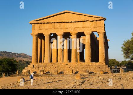 Agrigento, Sicily, Italy. West front of the Temple of Concordia lit by the setting sun, lone visitor looking up in awe, Valley of the Temples. Stock Photo