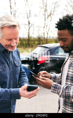 Younger and older drivers at side of the road exchanging car insurance details after traffic accident using mobile phones Stock Photo