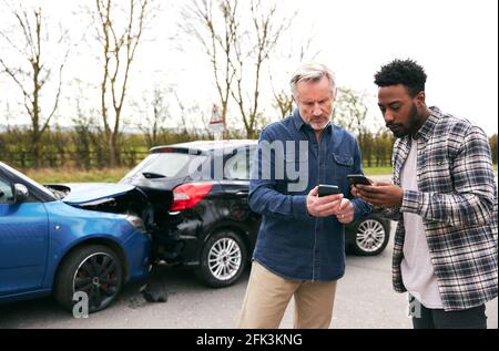 Younger and older drivers at side of the road exchanging car insurance details after traffic accident using mobile phones Stock Photo