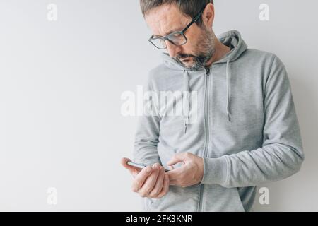 Casual man using mobile smart phone, leaning on the wall Stock Photo