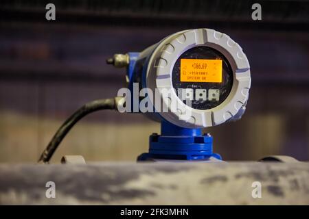 Close up photo of dirty electronic flow meter with digital display in factory workshop. Blurred background, low depth of field. Stock Photo
