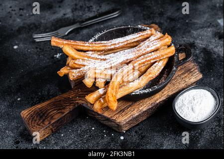 Traditional Mexican dessert churros with sugar powder in a pan. Black background. Top view Stock Photo