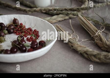 Craft white plate filled with gooseberries and red currants. Country rustic linen table set up Stock Photo