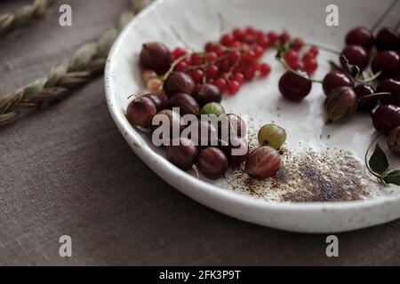 Craft white plate filled with gooseberries and red currants. Country rustic linen table set up Stock Photo