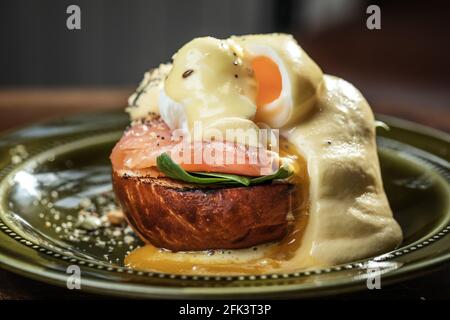 A serving of two Eggs Benedict, with  salmon, poached eggs and hollandaise sauce on a rustic green plate Stock Photo