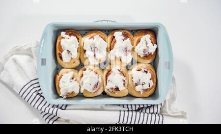 Flat lay. Glazing freshly baked cinnamon rolls in a blue baking pan. Stock Photo