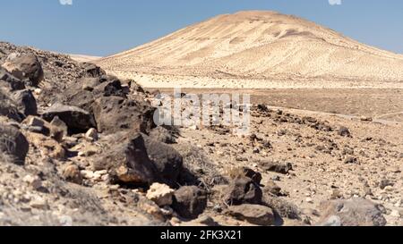 White hills dotted with black lava rocks in a desert landscape under a blue cloudless sky