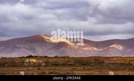 Sunlight falling through clouds in stripes on a mountain range at the horizon of a desert landscape Stock Photo