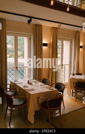 Rectangular table in the interior of a classic restaurant near high floor-to-ceiling windows overlooking the sea. Stock Photo