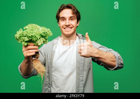Close up man holds salad and gives thumb up, isolated on green background Stock Photo