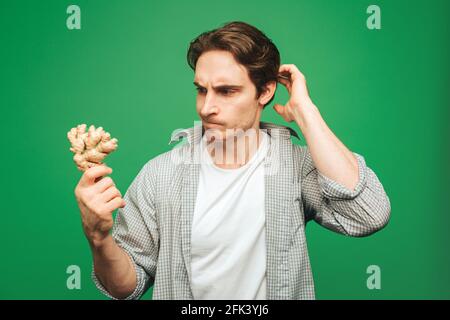 Young man holds curiously ginger, isolated on green background Stock Photo