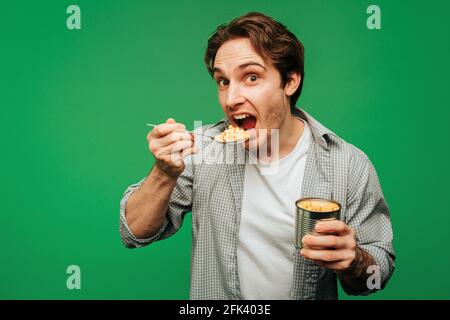 Young man eats corn in a jar, isolated on green background Stock Photo