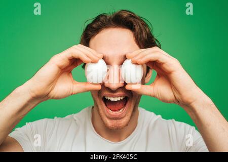 Young man covers eyes up by eggs, isolated on green background Stock Photo