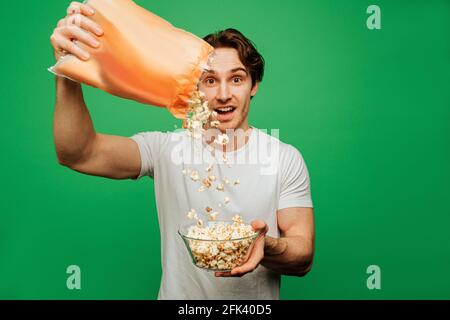 Young man happily pours popcorn into a plate, isolated on green background Stock Photo