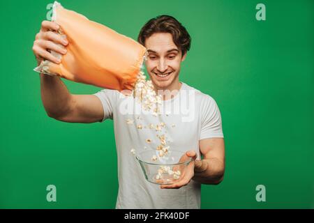 Young man pours popcorn into a plate, isolated on green background Stock Photo
