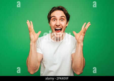 Young man looks surprised and happy, isolated on green background Stock Photo